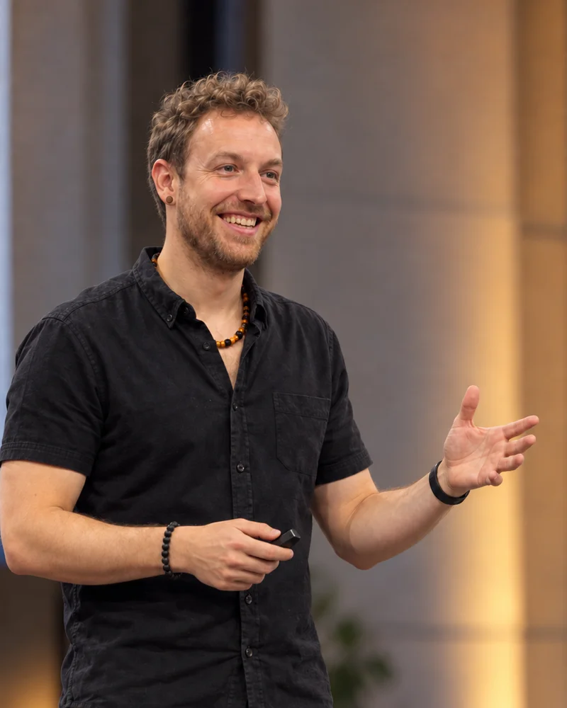 Olmo Romero de pie impartiendo una formación, sonriendo, con una mano abierta y el mando en la otra